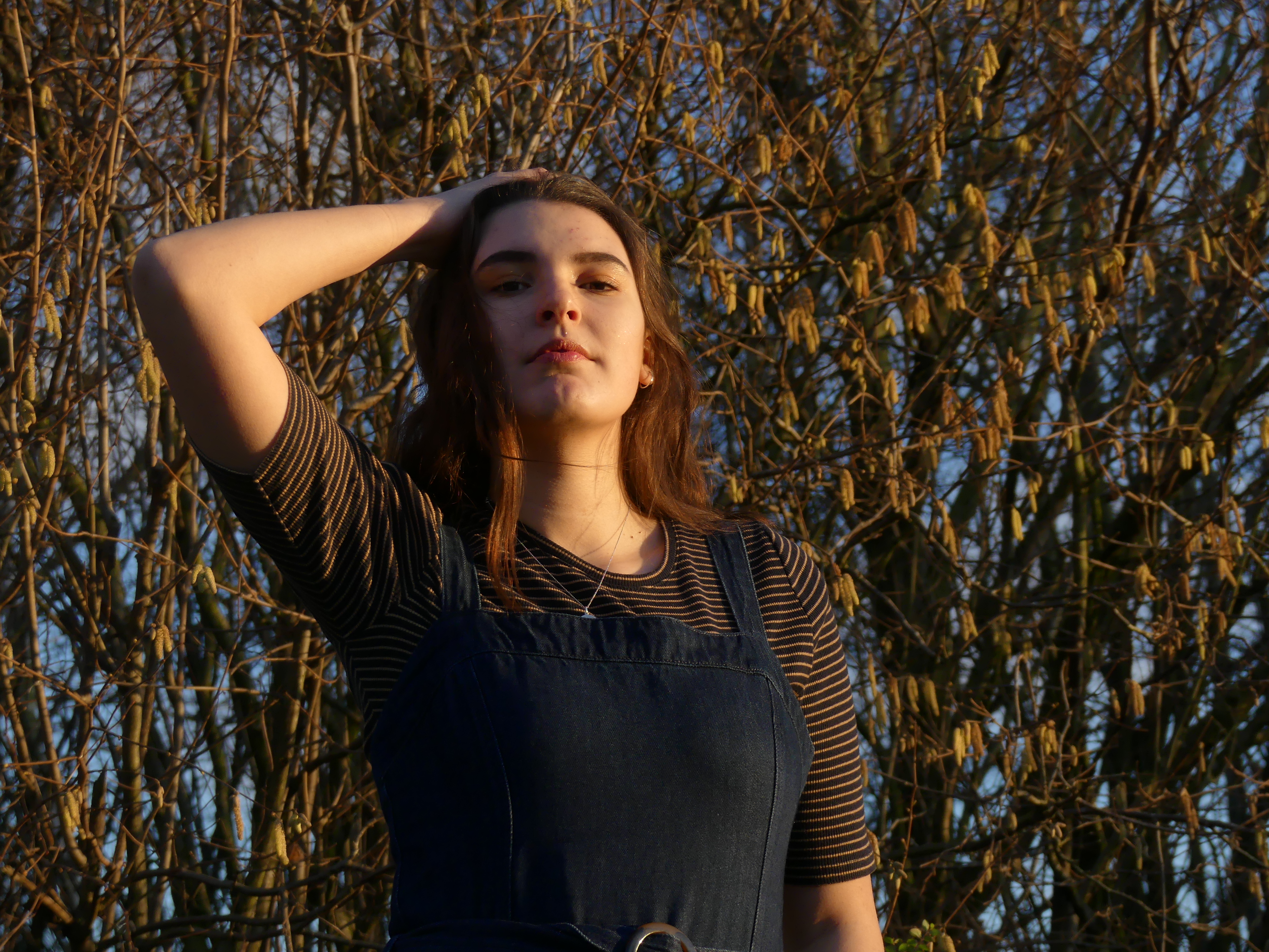 image of the model posed in sunlight against a backdrop of greenery