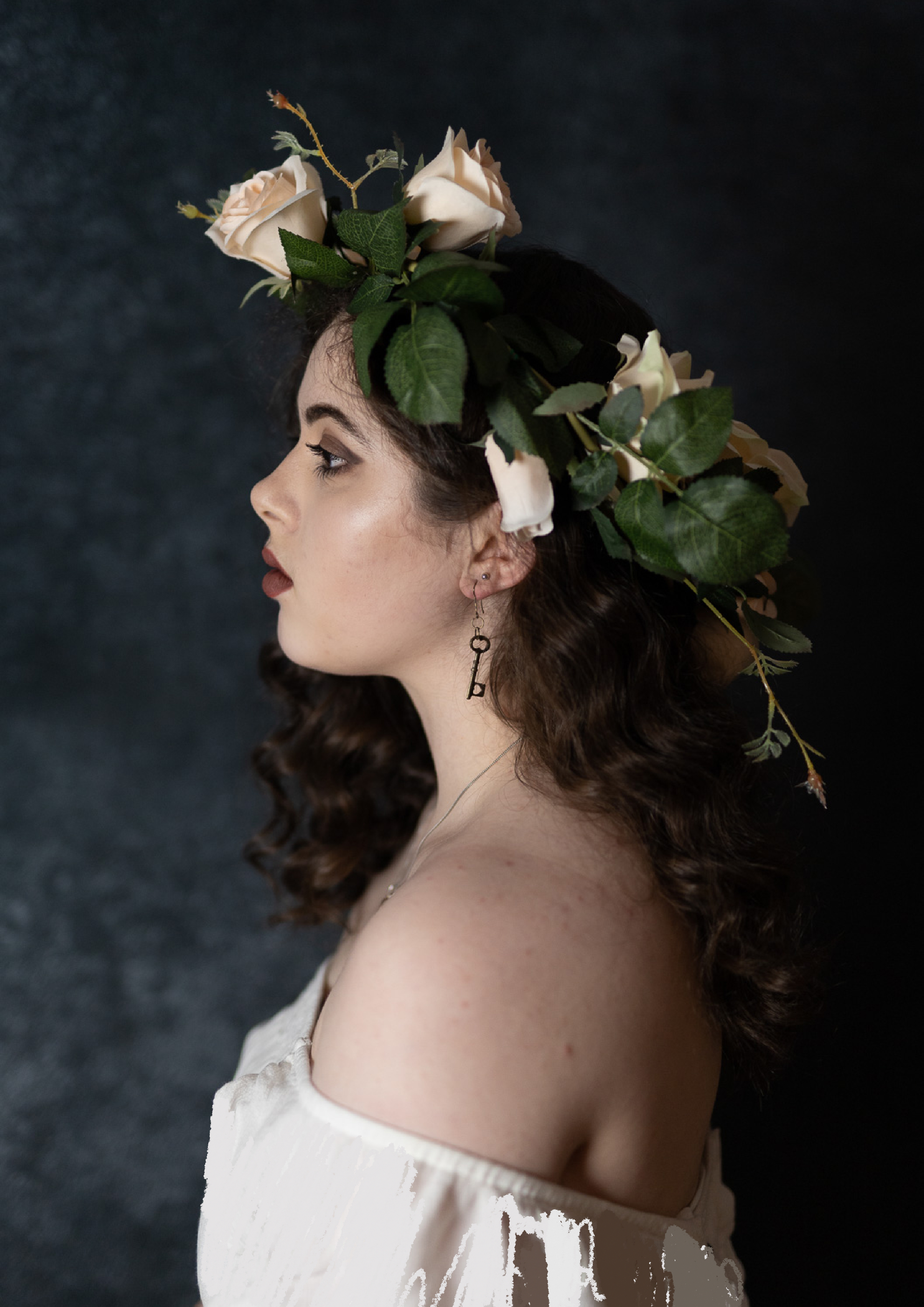 A side profile of myself wearing an off the shoulder white top and flower crown, looking away from the camera and against a navy blue background.